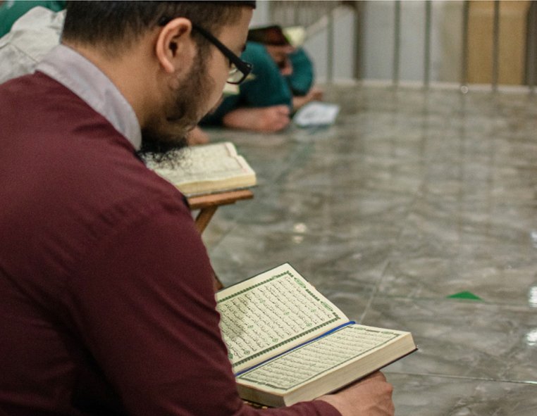 A student reading an open Quran while seated on a mosque floor
