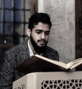 A young man reading the Quran from a wooden stand inside a mosque